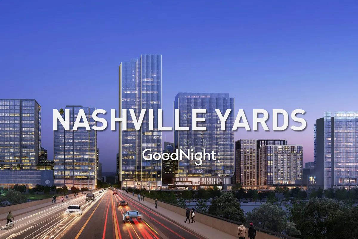 A dynamic city scene featuring tall, glass-covered office buildings illuminated against the night sky, with a busy roadway in the foreground. The setting evokes a sense of urban energy and is clearly located in a business district close to downtown action.