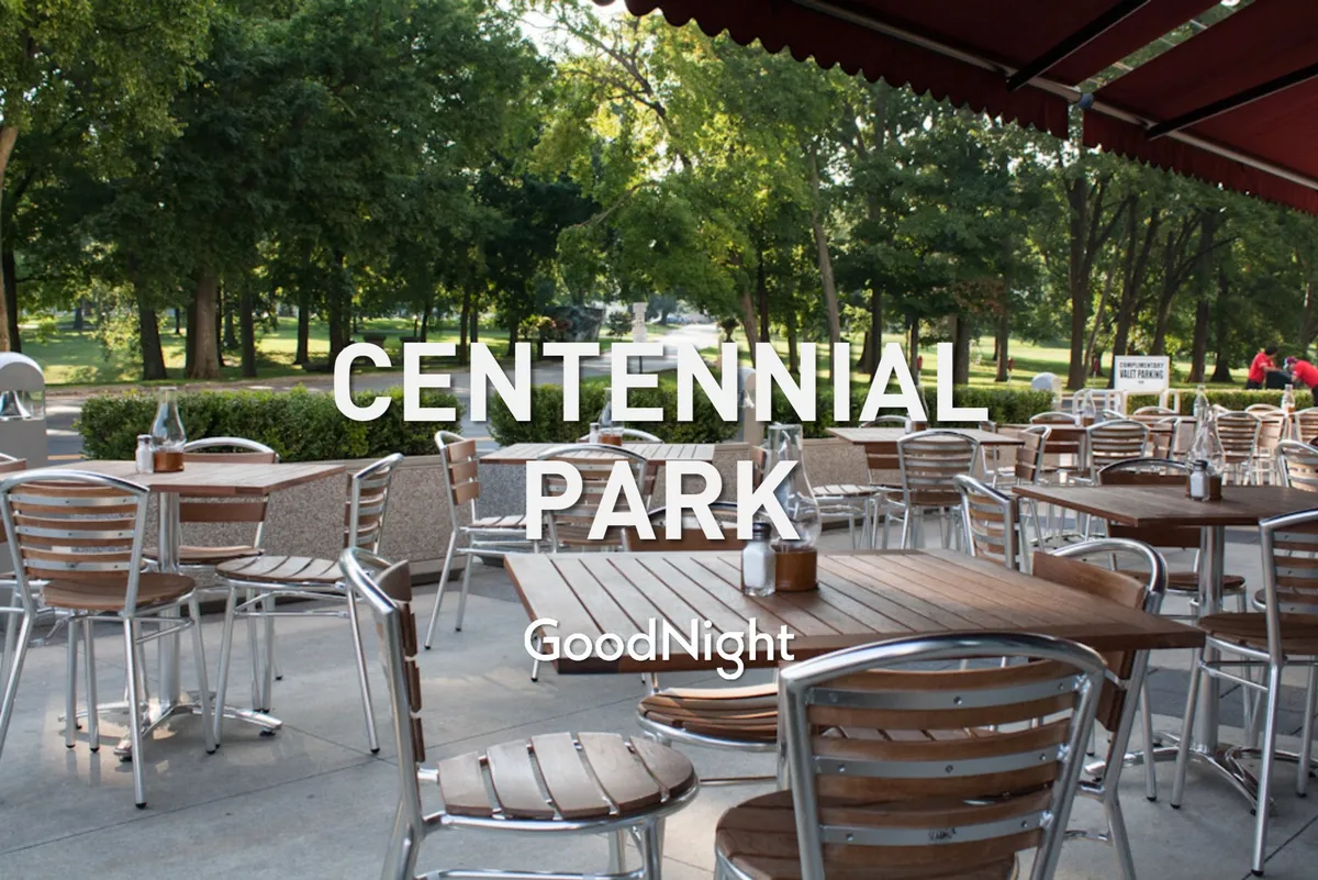 This image displays an inviting outdoor seating area surrounded by green trees, with wooden tables ideal for casual family dining or relaxing in nature. The setting is bright and approachable, suggesting a friendly, communal atmosphere.